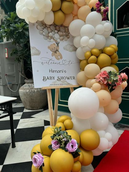 The welcome sign for Himani's baby shower, surrounded by a beautiful arrangement of white, gold, and peach balloons with floral accents.