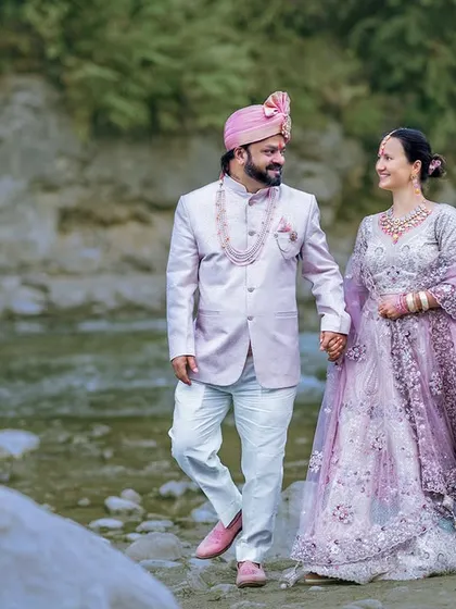 A royal walk by the riverside. The couple's elegant ethnic wear looks stunning against the rugged, natural backdrop of the river and green hills.