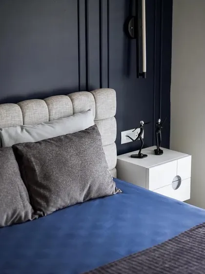 The guest bedroom is a study in tranquility, with deep blue walls featuring minimal moulding. The plush, upholstered bed and quality linens create a relaxing and inviting atmosphere for guests.