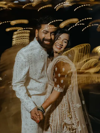 A joyful, candid shot of the couple laughing, with motion blur from the surrounding lights adding to the dynamic energy of the reception.