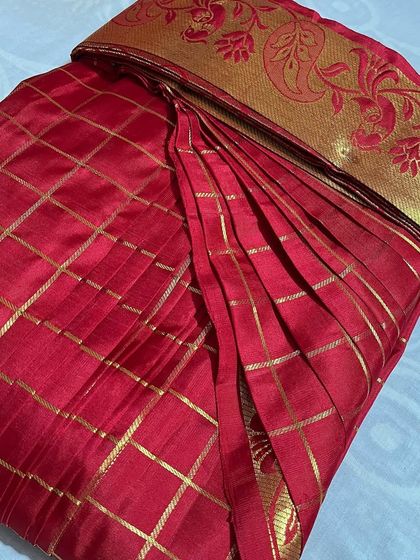 A bright red checked silk saree with a floral border. The pleats are neatly done to maintain the pattern's alignment.