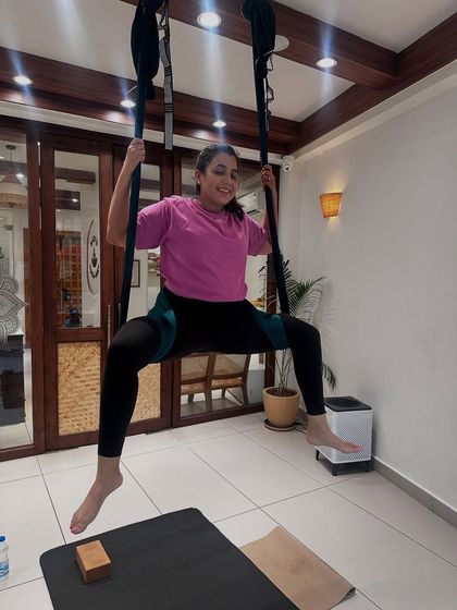 A student smiles as she masters a challenging seated pose in the aerial hammock, demonstrating the strength and balance she has developed through her practice.