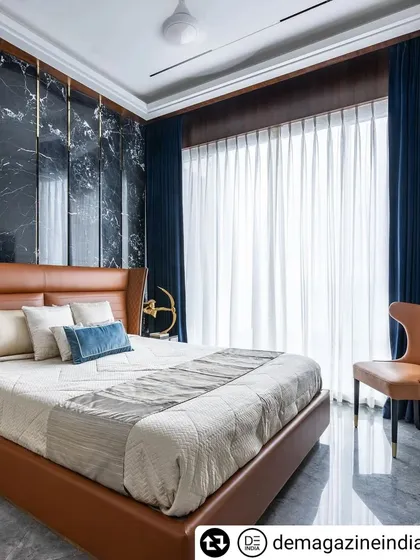 The master bedroom in the 'Fifty Two' apartment features a dramatic black marble wall with gold inlays behind a tan leather bed. The deep blue curtains add to the room's rich, royal aesthetic.