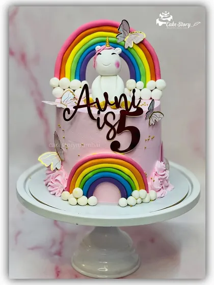 A magical unicorn and rainbow cake for a 5th birthday. This design features a fondant unicorn sitting happily under a big rainbow, surrounded by clouds and butterflies.