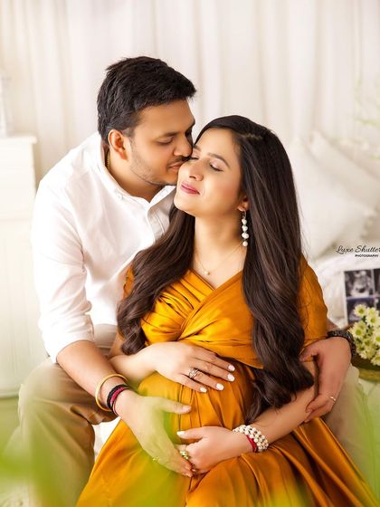A sweet kiss on the cheek. This candid-style shot captures a genuine moment of affection between the expecting parents in a beautifully lit setting.
