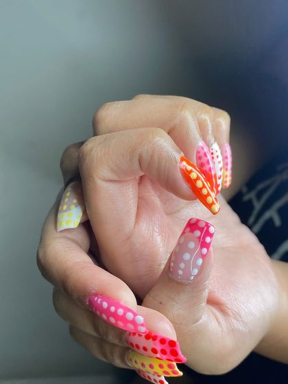 A dramatic and colorful set of long nails with a multi-color gradient and white polka dots.