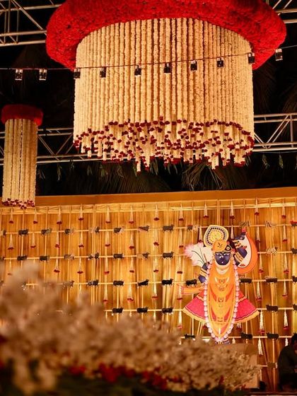 A unique stage backdrop featuring a traditional Indian deity motif and hanging floral chandeliers made of jasmine and roses. This decor beautifully blends cultural elements with grand design.