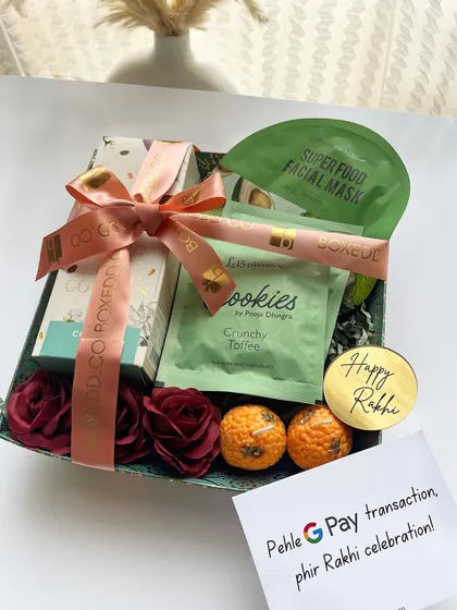 A fun and sweet Rakhi hamper for a sibling, complete with cookies, a face mask, and a cheeky note that says "Pehle G Pay transaction, phir Rakhi celebration!"