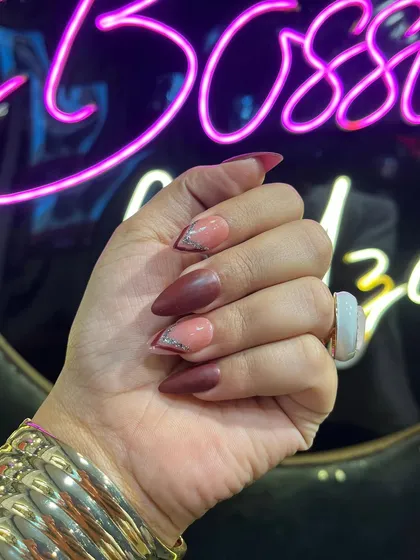 A closer look at this custom stiletto nail art, showcasing the clean lines and the contrast between the matte red-brown polish and the sparkling silver glitter accent.