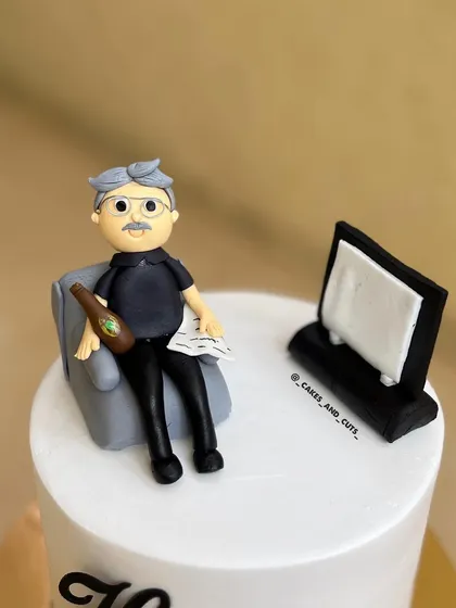 A close-up of the fondant figurine we created for a 76th birthday cake, showing a grandpa relaxing with a drink and the newspaper.