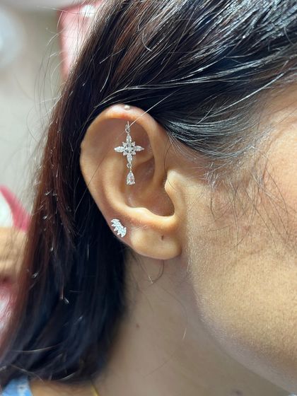 This delicate silver stack features a cross-shaped hanging and a leaf-like stud, creating a look that is both graceful and modern.