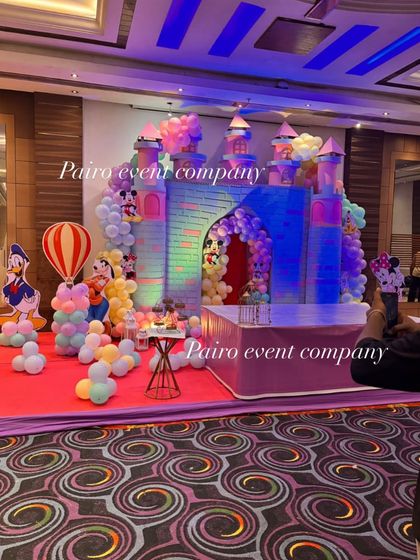 The same castle theme decoration, showing the full stage setup. The lighting enhances the colors of the castle and the pastel balloon arrangements.