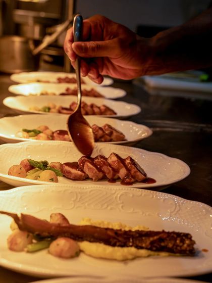 A chef saucing a line of plates, adding the finishing touch to a dish.