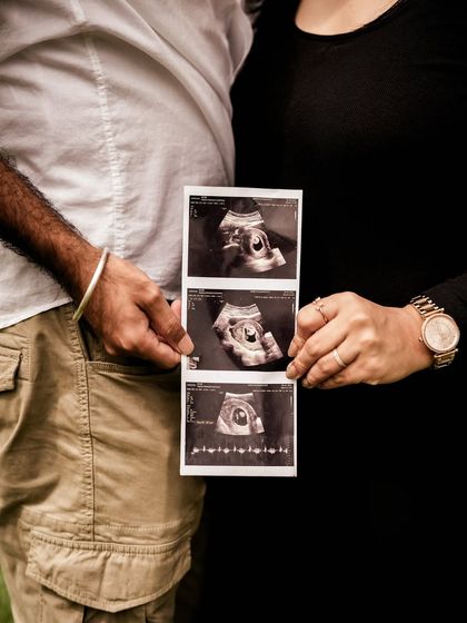 A warm-toned monochrome close-up of the couple holding the sonogram pictures. The focus is on their hands and the first images of their baby.