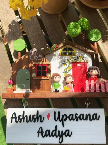 Your whole family can be part of the story. This custom family name sign includes adorable miniatures for the parents and their child, set in a colorful little scene. The hanging name board below adds a lovely touch, making it a complete and personal welcome for your home.