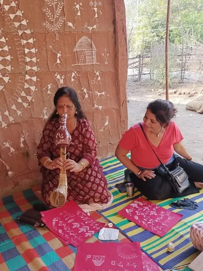 An instructor and student work side by side against a backdrop of authentic Warli wall art. This retreat offers a rare opportunity to learn in a truly immersive setting.