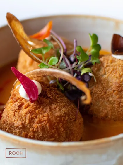 A close-up of the Tofu & Edamame Kofta, served in a light, flavourful curry and garnished with vegetable crisps. A delightful vegetarian main course.