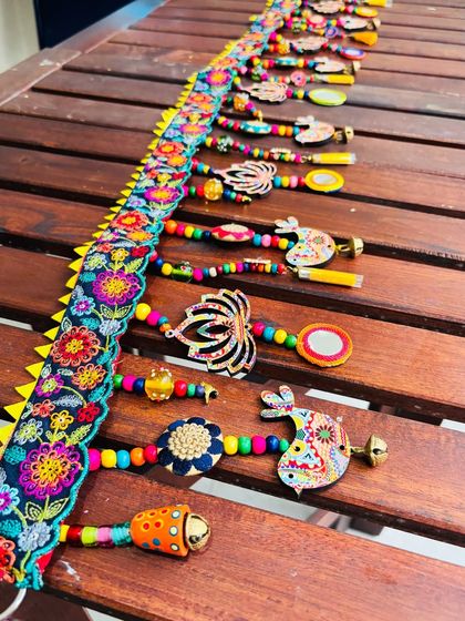 A close-up of the 'Tamaara' toran, highlighting the delicately embroidered lace topper and the mix of sustainable embellishments. You can see the wooden beads, metal floral buttons, and my original artwork on the cutouts.