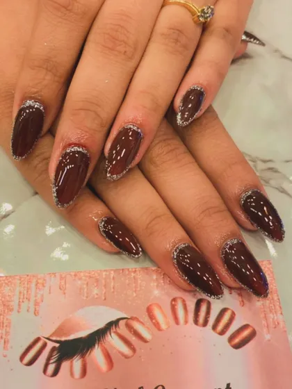 An elegant and subtle take on glitter nails. This design features long, almond-shaped extensions with a deep maroon polish and a delicate silver glitter outline along the tips.