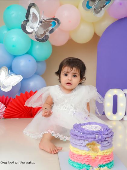 A wider view of the butterfly-themed first birthday setup, with a beautiful pastel balloon arch and a "ONE" marquee sign.