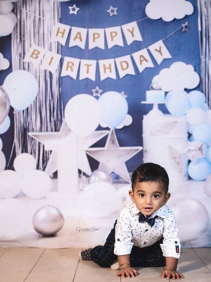 A dreamy first birthday setup with a "Happy Birthday" banner and a sky full of stars and clouds. The blue and silver color scheme is perfect for a "twinkle twinkle little star" themed shoot.