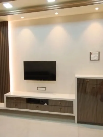 A simple yet elegant TV unit design. The combination of dark wood fluting, a clean white console, and warm spotlights creates a balanced and modern look for the living room.