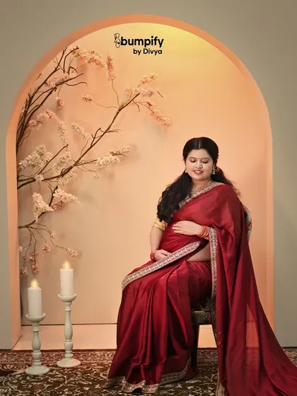 A serene solo portrait of the mom-to-be seated in our warm, floral arch setup. The red of her saree creates a beautiful contrast with the soft, neutral background.