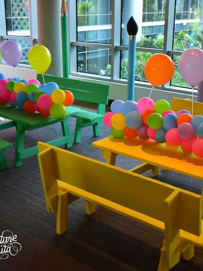 The kids' seating area featured colourful picnic benches and balloon runners. The giant pencil and paintbrush props at the ends of the tables add a fun, oversized element.