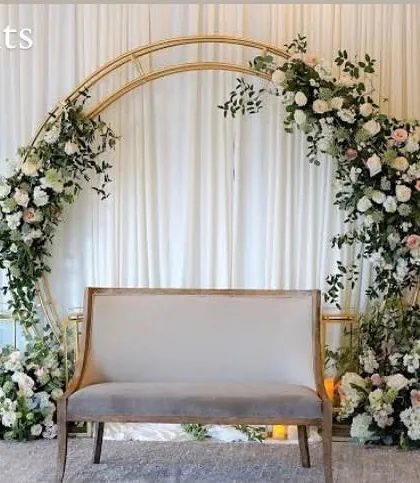 I created this elegant and romantic backdrop for an engagement ceremony. A golden double-ring arch is lavishly decorated with white roses and cascading greenery, with a simple, classic loveseat placed in front for the couple.