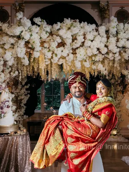 A classic portrait with a touch of grandeur. The groom holding his bride, framed by a stunning floral mandap, creates a timeless and romantic wedding photograph.