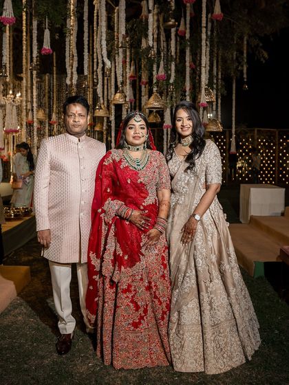 A formal portrait of the bride with her brother and sister-in-law. We styled the sister-in-law in a sophisticated beige lehenga that beautifully complements the bride's red wedding attire.