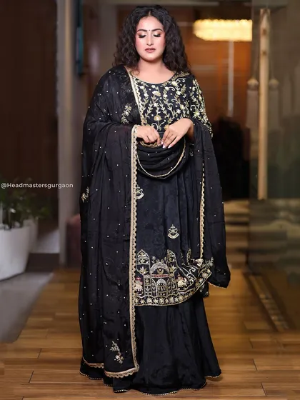 A full-length view of the black and gold ethnic wear look. The makeup is kept glamorous and glowing to complement the dark, embroidered outfit.