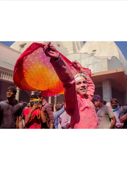 A young man dances with a colorful scarf during Holi, a bright smile on his face. This shot captures the pure joy and uninhibited spirit of the celebration.
