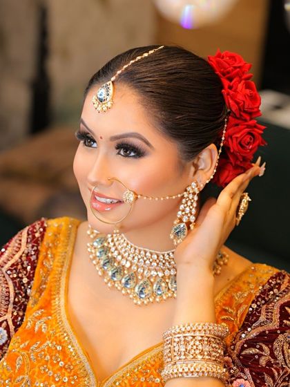 This bride is radiating pure elegance. The look features a classic red rose bun, bold eyeliner, and glowing skin, perfectly complementing her yellow and red bridal attire.