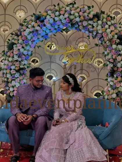 A beautiful floral arch in shades of lavender and pink creates a perfect backdrop for an engagement ceremony, complementing the couple's attire.