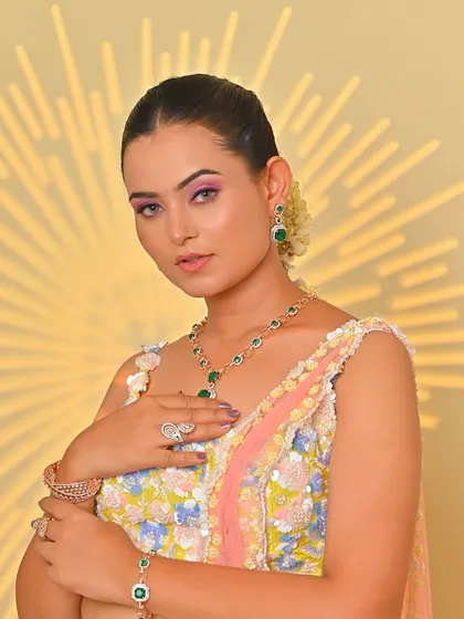 A modern Haldi look with a pastel lehenga and emerald jewelry. The makeup is soft and glowing, with a pop of color on the eyes.