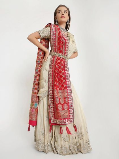A beautiful blend of subtle and bold. This hand-embroidered ivory lehenga gets a vibrant pop of color from a traditional red Bandhani dupatta, creating a look that's both classic and fresh.