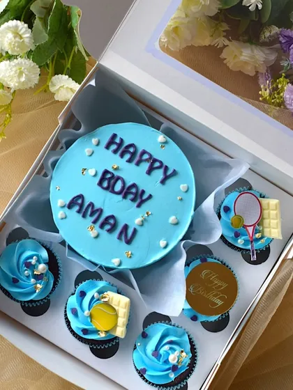 A close-up of the "Happy Bday Aman" bento cake. You can see the small heart sprinkles and the detailed decorations on the cupcakes, including a tiny tennis ball and racket.