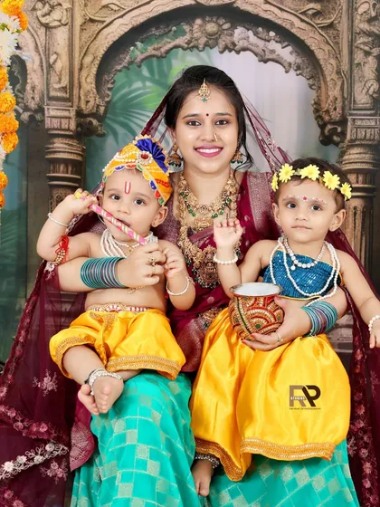 Double the cuteness in this Radha-Krishna themed shoot. A mother holds her two little ones, both dressed in adorable traditional costumes, creating a vibrant and memorable portrait.