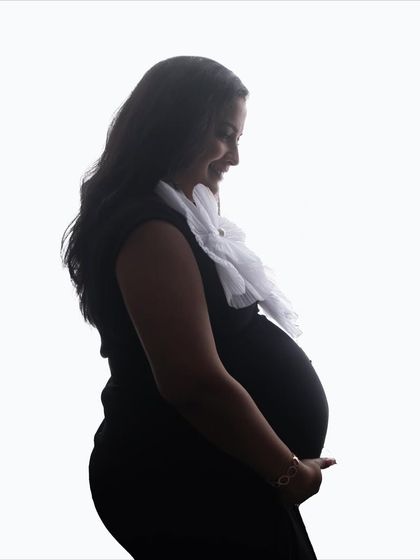 A simple and gentle silhouette portrait. The mom-to-be's soft smile is captured as she looks down, creating a feeling of quiet joy and anticipation.