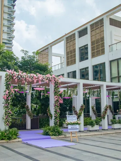 A beautiful floral entrance to an engagement party, with a purple carpet and a pergola structure adorned with pink flowers and hanging umbrellas.
