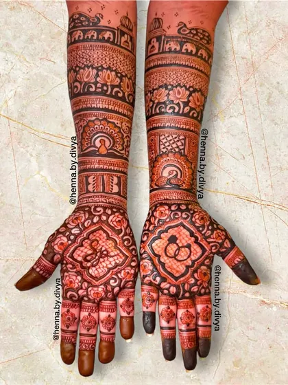 An intricate engagement mehendi extending up the arms. The palms feature the initials 'JB' and an engagement ring symbol, while the arms have detailed traditional patterns.