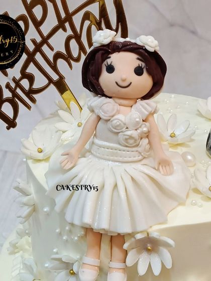 An elegant two-tier pineapple cake for a second birthday. This all-white design features a fondant princess doll, a pet figure, and is adorned with delicate white fondant flowers.