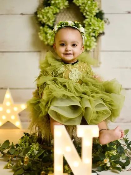 Turning one is a big deal. This setup uses marquee lights spelling "ONE" and a beautiful rustic theme to celebrate the milestone. The little girl's olive green dress and happy smile complete the perfect first birthday photo.