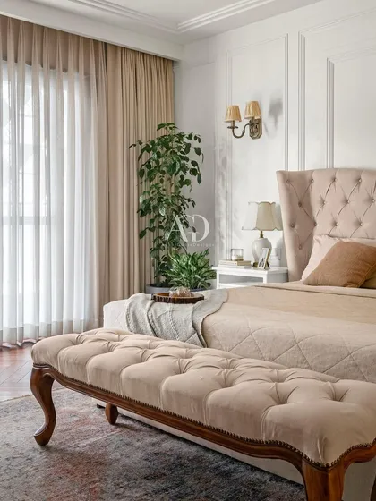 This bedroom corner showcases careful planning and craftsmanship. The tufted, winged headboard in a soft beige fabric creates a sense of comfort and luxury, complemented by the rich herringbone wood flooring.