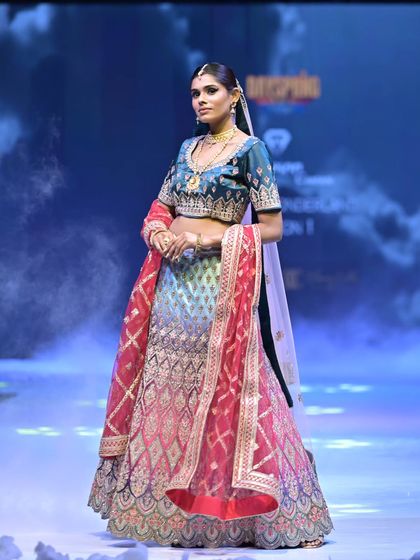 This unique lehenga features an ombré skirt that transitions from blue to pink, all covered in intricate silver embroidery. The deep teal velvet blouse adds a touch of modern luxury.
