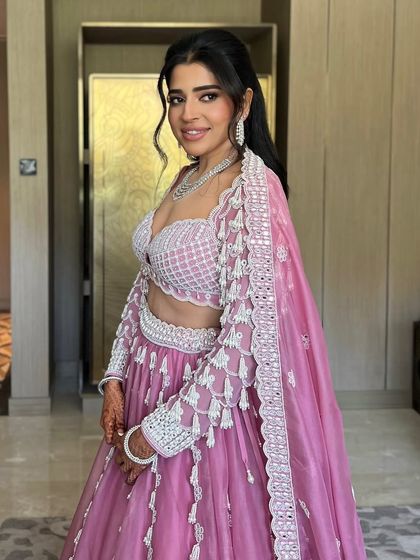 A bride in a lovely pink outfit, her long, dark hair styled in simple, elegant waves.