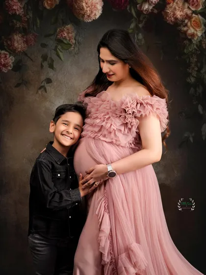 Welcoming a new sibling is a special time. This portrait captures a proud big brother with his hand on his mother's baby bump, set against a romantic floral arch.