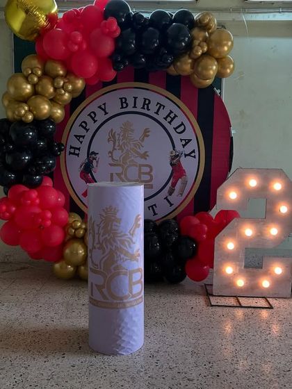 A closer view of the RCB-themed birthday decor, highlighting the custom backdrop and the striking red, black, and gold balloon colors.