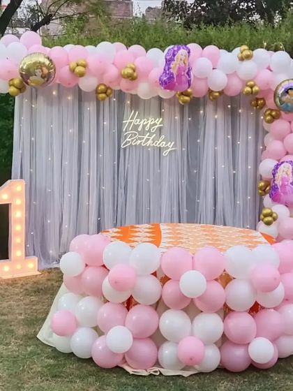 A princess-themed first birthday party set up on a lawn, with a full balloon arch and decorated table.